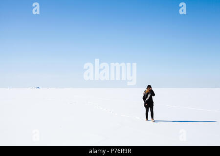 Woman in Black marche sur la mer Baltique gelée sous ciel d'hiver bleu vif Banque D'Images