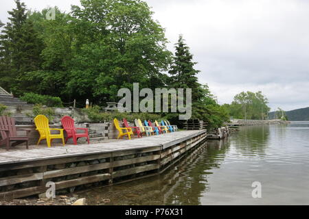 Une rangée de chaises Adirondack multi-couleur sur le bord de lac à Baddeck, sur les rives du lac Bras d'Or, Nouvelle-Écosse, Canada Banque D'Images