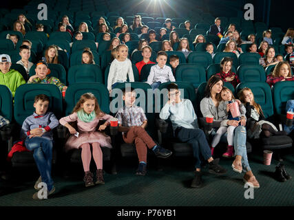 Vue de face de nombreux enfants et adolescents assis dans un cinéma et profiter de caricature. Cute little girl sitting on her mother tours. Spectateurs expre Banque D'Images