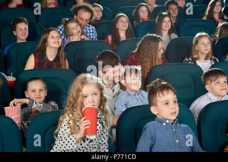 Avis des spectateurs regarder film et rire dans le cinéma.Des Enfants assis sur leurs pères tours, smiling, eating popcorn, boire des boissons gazeuses. Concep Banque D'Images