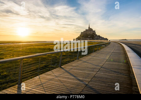 Vue sur le Mont Saint-Michel, l'île de marée en Normandie, France, au coucher du soleil avec la jetée en bois au premier plan. Banque D'Images