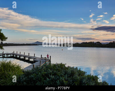 Un pêcheur solitaire debout sur un ponton de Bellinger River dans la soirée avec le soleil commence à définir à Mylestom, Mi côte nord Région, l'Australie Banque D'Images