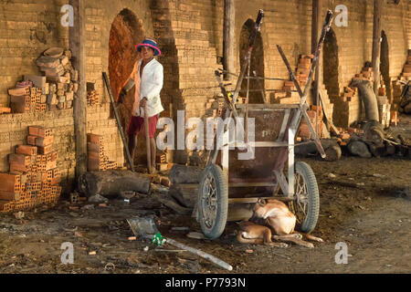 Un brickworker cambodgienne du nord tend les fours, avec son chien à proximité. Banque D'Images