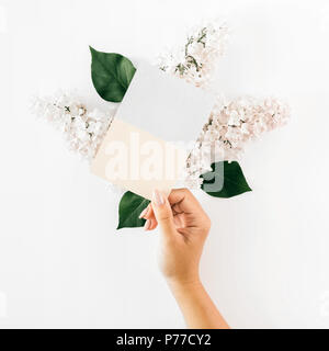 Vue supérieure de la femme hand holding carte vierge sur fond blanc avec la branche de lilas blanc. Mise à plat Banque D'Images