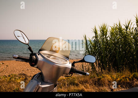 Un vélo scooter argent générique est garé au bord de la mer. La plage tropicale et les vacances d'été.Maison de concept. Louer une voiture, vélo, tout transport pour vos vacances.Copy space.Vue depuis le siège du conducteur. Banque D'Images