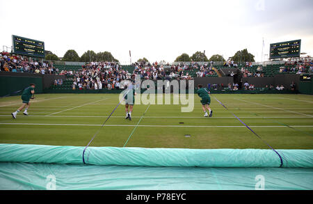 Le personnel au sol tirer la cour s'étend sur plus de trois que la pluie cesse de jouer sur la troisième journée du tournoi de Wimbledon à l'All England Lawn Tennis et croquet Club, Wimbledon. Banque D'Images