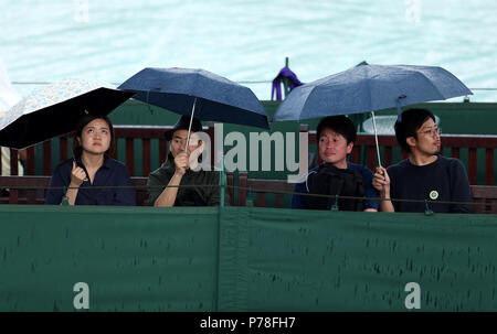 Les spectateurs à l'abri sous les parasols pendant un Rain Delay sur la troisième journée du tournoi de Wimbledon à l'All England Lawn Tennis et croquet Club, Wimbledon. Banque D'Images