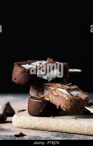 Libre d'un peu de chocolat barres de crème glacée sur une planche à découper, placé sur une table rustique en bois sombre, sur un fond noir avec quelques espaces vides o Banque D'Images