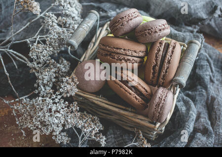 Des petits macarons dans panier en osier avec poignées avec petites fleurs blanches sur fond de bois. Focus sélectif. Banque D'Images