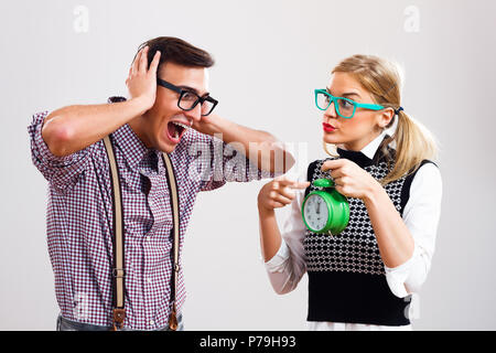 Femme nerdy montrant réveil à son petit ami nerdy. Banque D'Images