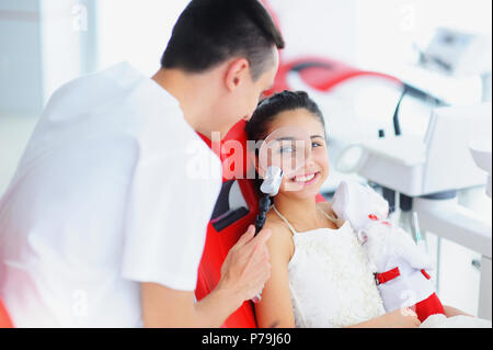Beau sourire avec des dents blanches. Un dentiste examine la cavité orale d'une jeune fille belle à travers une loupe dans le cabinet dentaire. Banque D'Images