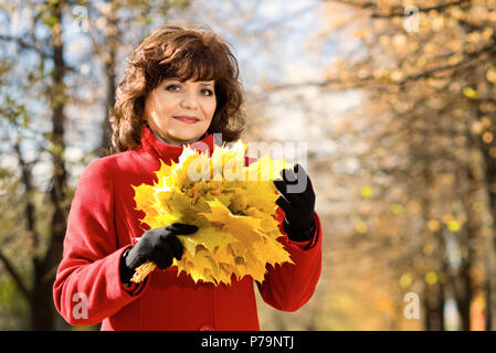 La belle mature woman in red topcoat, piscine dans parc, journée d'automne Banque D'Images