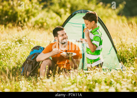 Père et fils sont en camping dans la nature. Ils mangent. Banque D'Images