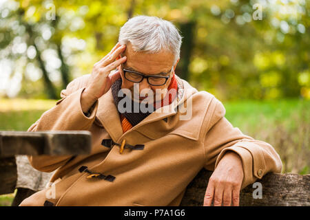 Senior man sitting in park et avoir des maux de tête. Banque D'Images
