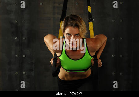 Une jeune femme athlétique à la formation, l'entraînement avec crossfit trx suspension sangles de remise en forme sur fond sombre, vue de face, looking at camera Banque D'Images