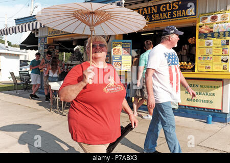 Geneva-On-The-Lake, USA. 4 juillet, 2018. Femme est titulaire d'un parasol pour tempérer la chaleur extrême en marchant le Geneva-On The-Lake-bande sur le 4 juillet 2018 maison de vacances. Le couple passe devant le capitaine Gus' Shake Shack et Sandwich, l'un des nombreux établissements de restauration le 4 juillet 2018 les foules dans ce resort ville célébrant le jour de l'indépendance. Nous Mark Kanning/Alamy Live News Banque D'Images