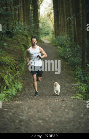 Man jogging avec son chien dans la forêt luxuriante Banque D'Images