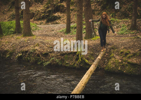 Female hiker marche sur le tronc d'arbre tombé de l'autre côté de la rivière Banque D'Images