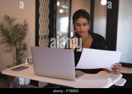 Businesswoman reading documents alors working on laptop Banque D'Images