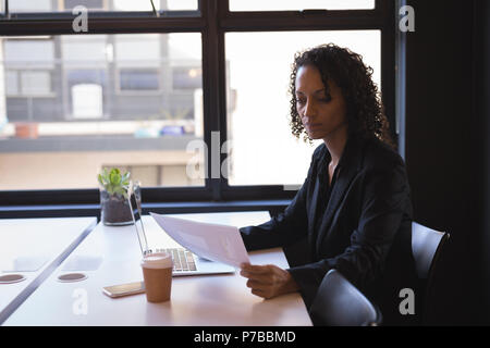 Businesswoman reading documents alors working on laptop Banque D'Images