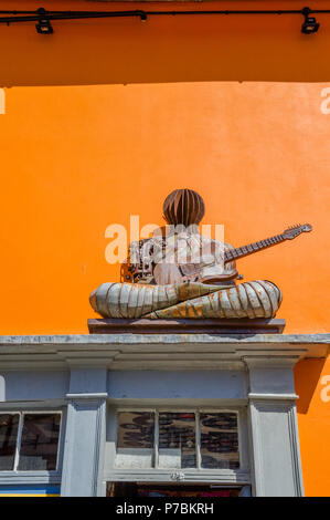 Sculpture de métal d'un musicien pattes avec guitare était assis sur un cadre de porte. Banque D'Images