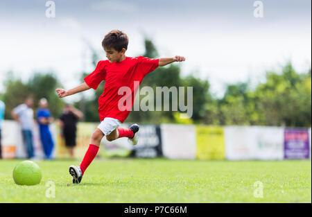 Boy kicking soccer ball sur le terrain de sport Banque D'Images