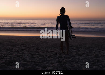 Fit woman holding surfboard in la plage au crépuscule Banque D'Images