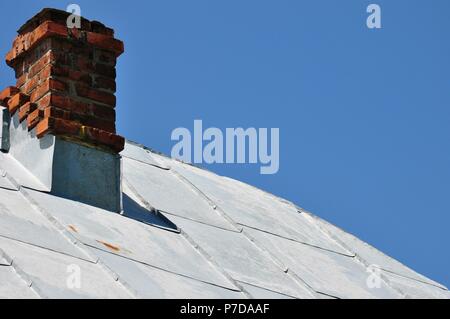 Toit en métal gris feuille avec une cheminée traditionnelle place dans le coin en haut à gauche sur une vieille maison à la campagne, avec un fond de ciel bleu clair, cop Banque D'Images