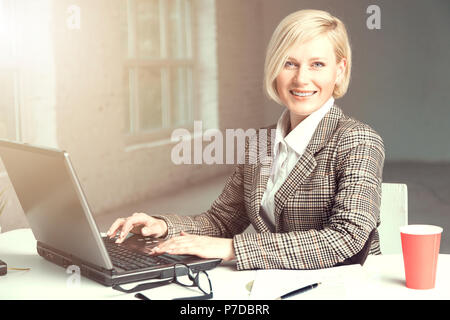 Belle blonde adult businesswoman habillés en costume élégant vérifié en travail social à l'échelle blanche sur table with laptop Banque D'Images