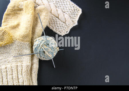 Une balle de laine avec des aiguilles à tricoter et de chaussettes sur un tableau gris. La couture Banque D'Images