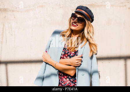 Femme élégante portant des lunettes de soleil et capuchon en avant du mur avec les bras croisés Banque D'Images