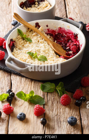 Recette traditionnelle pour berry crumbble à partir de baies de cassis, framboises et bleuets close-up dans une casserole sur une table verticale. Banque D'Images