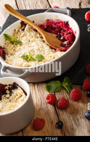 Crumble aux baies de cassis, framboises et bleuets décoré à la menthe close up sur la table. vertical Banque D'Images