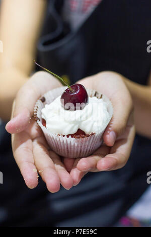 'Cupcake Red Velvet' blanc avec crème fouettée et des cerises dans les mains du cuisinier Banque D'Images