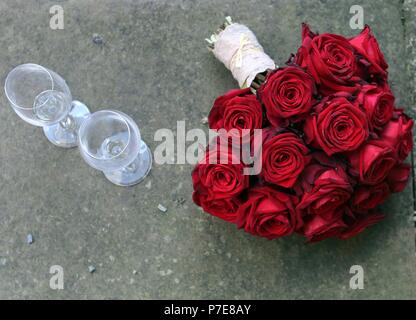 Bouquet de mariée avec roses rouges à côté des verres à vin Banque D'Images