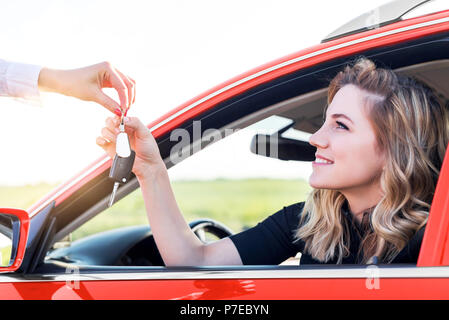 Une jolie femme dans une voiture obtient les clés de voiture. Louer ou acheter de l'auto. Banque D'Images