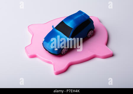 Petite voiture bleue sur télévision Pink Piggybank isolé sur fond blanc Banque D'Images