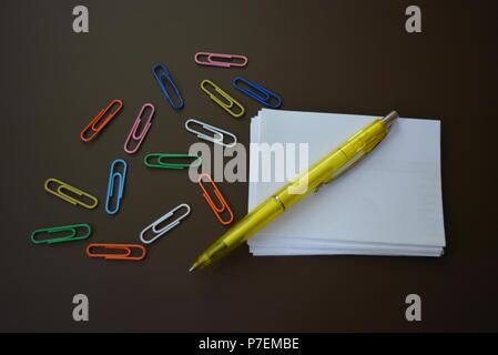La couleur des trombones de couleurs différentes avec des feuilles de papier blanc pour l'enregistrement et un stylo jaune brun sur un fond mat. Banque D'Images