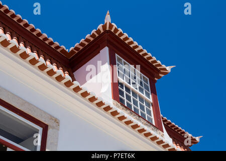 Détail d'une maison portugaise. Toit avec de nouvelles tuiles et une fenêtre. Nids d'hirondelle. Ciel bleu clair lumineux. Castro Marim, Algarve, Portugal Banque D'Images