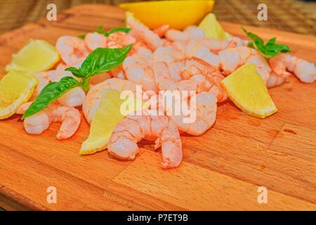 Crevettes cuites et décortiquées avec des tranches de citron et feuilles de basilic sur planche à découper. La photographie culinaire. Alimentation saine. Recette Bio. Banque D'Images