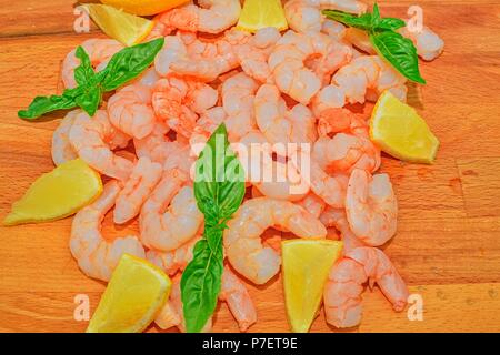 Crevettes cuites et décortiquées avec des tranches de citron et feuilles de basilic sur planche à découper. La photographie culinaire. Alimentation saine. Recette Bio. Modèle plat. Banque D'Images