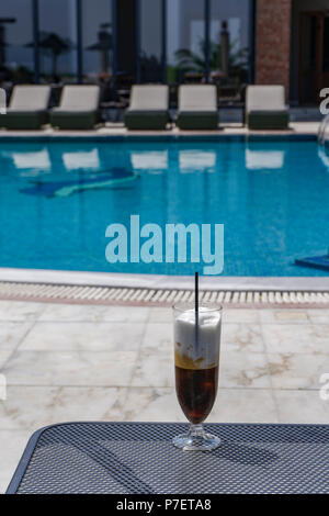 Café glacé sur un verre avec paille en plastique. Freddo cappuccino servi en Grèce avec piscine floue fond. Banque D'Images