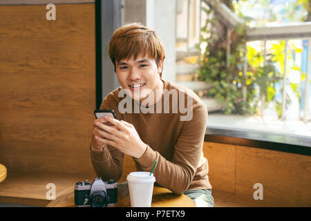 Young Asian man using smart phone pendant le petit-déjeuner, le café et le temps des vacances locations de concepts Banque D'Images