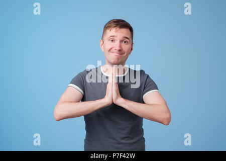 Beau jeune homme en bleu t-shirt pressages paumes ensemble et à la caméra, à la mendicité pour le pardon Banque D'Images