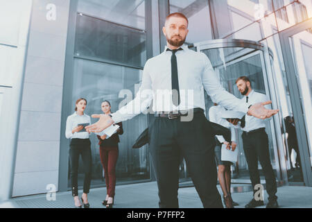 En faillite. Un jeune homme en pantalon noir et une chemise blanche démontre ses poches vides à l'arrière-plan d'un groupe d'employés de bureau. Licenciement bof Banque D'Images