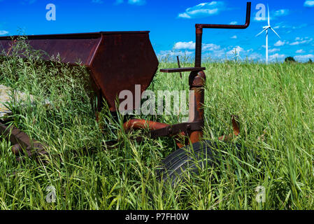 L'agriculture Vintage herse à disques dans un champ entouré de hautes herbes aux éoliennes à l'extérieur de Swift Current, Saskatchewan, Canada Banque D'Images