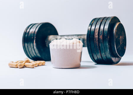 La poudre de protéine de lactalbumine dans une boule à côté de tas de comprimés de vitamines et old rusty haltère sur un fond blanc. Suppléments de nutrition sportive et lourd weig Banque D'Images