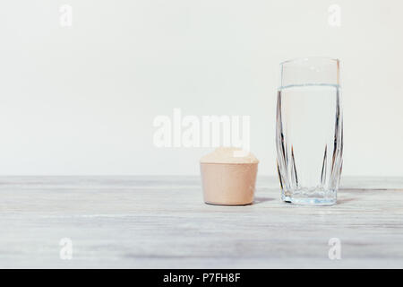 Boule de protéines en poudre supplément sportif à côté d'un verre de l'eau propre sur un tableau blanc en bois. Banque D'Images