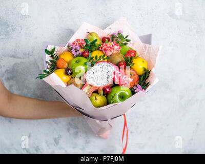 Bouquet de fruits et de baies. Bouquet de manger dans la main des femmes sur fond gris. Apple, orange, fraise, poire, kiwi, fruit du dragon et de fleurs, l'eucalyptus Banque D'Images