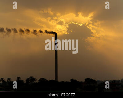 Coucher de soleil sur le Nil en Égypte, dans une zone industrielle avec la pollution causée par l'augmentation spectaculaire de la cheminée fumer couleurs orange dans les nuages Banque D'Images